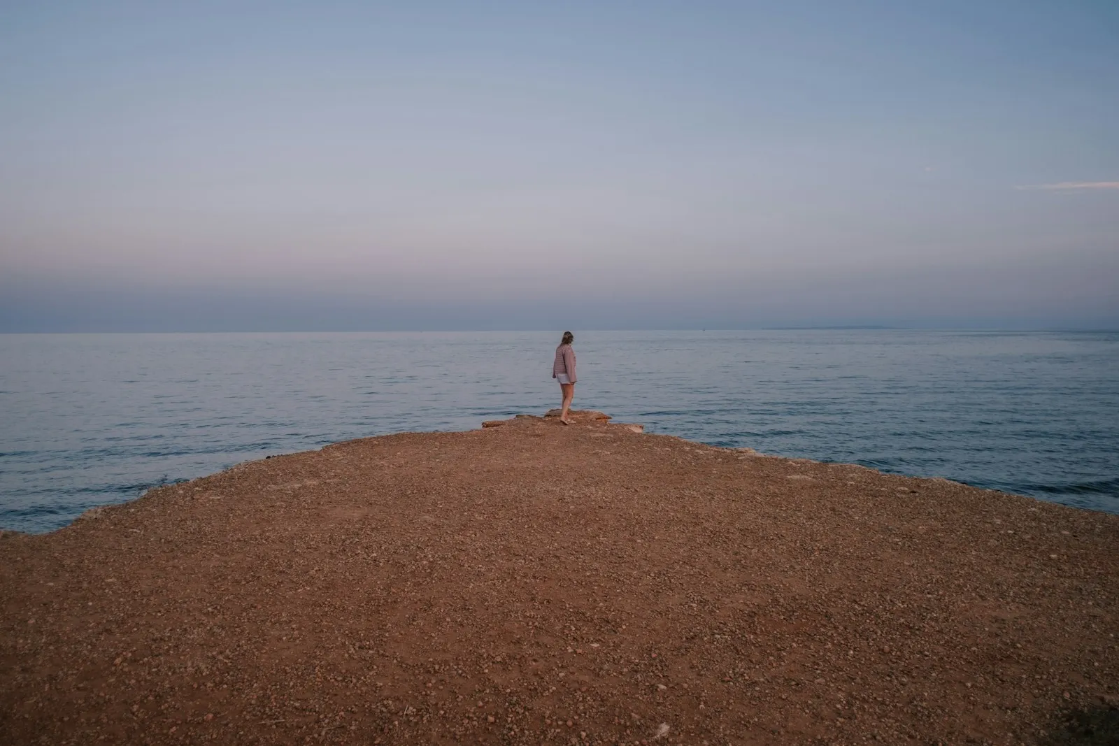 Une femme seule au bout d’une avancée de terre face à la mer, immobile avant de faire un pas