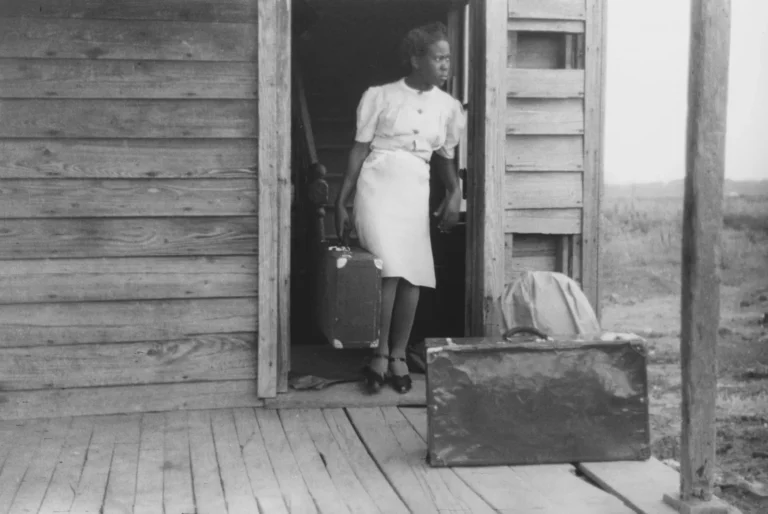 Une femme sur le pas d’une porte, une valise à la main, prête à partir, photo en noir et blanc