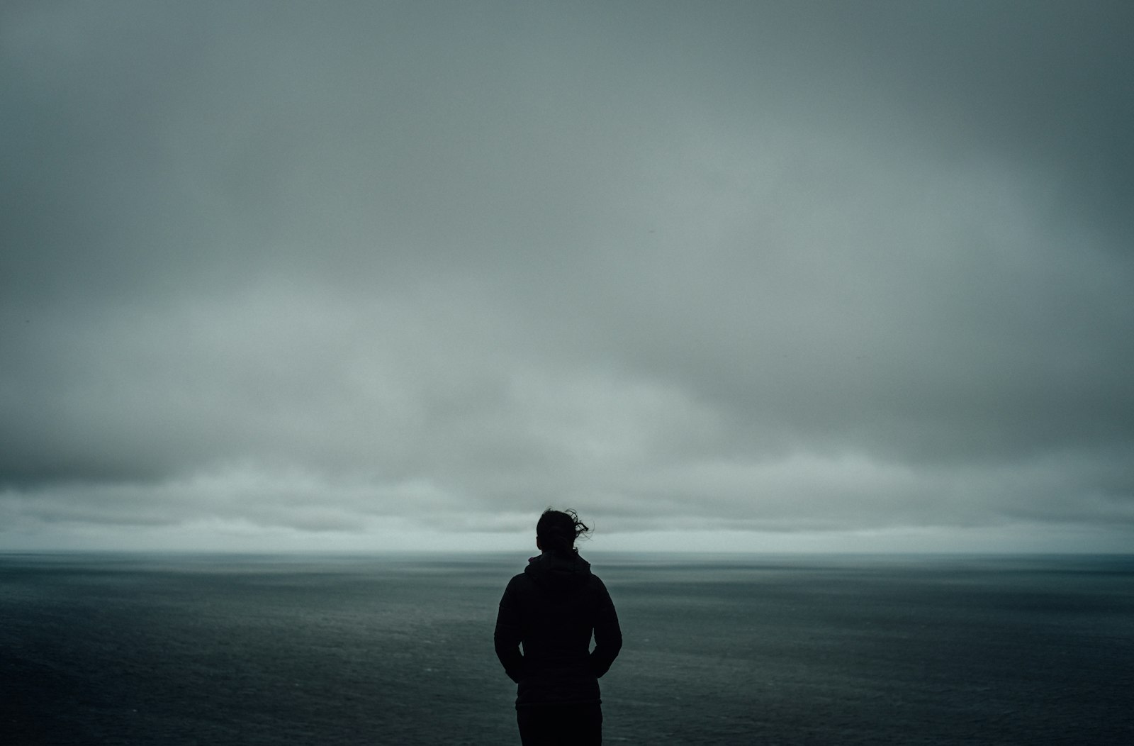 Silhouette seule face à une mer grise sous un ciel chargé